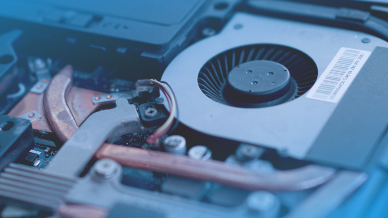 Close-up view of a laptop's internal cooling system, showing a blower fan, copper heat pipes, and surrounding components inside the chassis.
