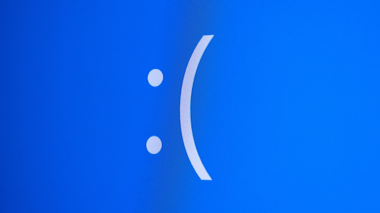 Close-up of a blue computer error screen displaying a large white sad-face emoticon, commonly associated with the Windows "Blue Screen of Death."