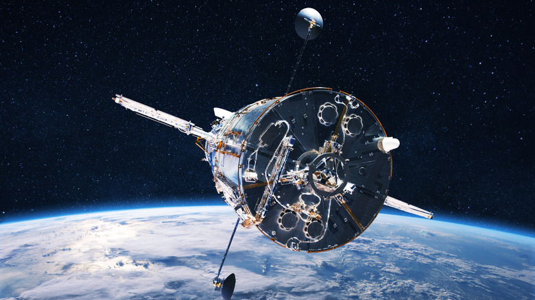 Satellite orbiting above Earth with antennas and solar equipment visible.