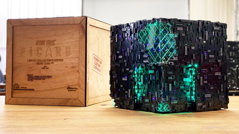 A computer shaped like a Borg cube from Star Trek, a black cube with glowing green areas. It sits next to a crate with the Star Trek: Picard logo.