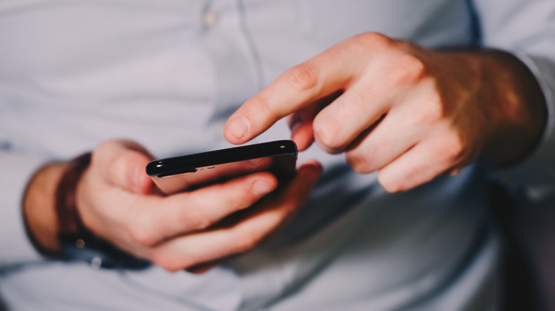 Close up of a man's hands holding an Android phone with one hand and swiping the screen with the other.