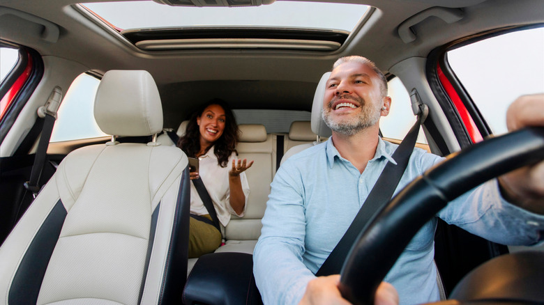 A driver looking at the rear-view mirror with a person sitting at the back