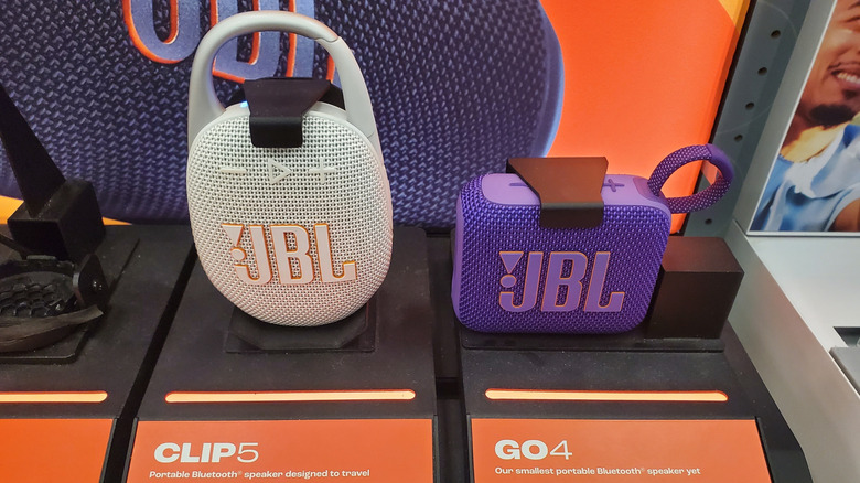 JBL Clip 5 and JBL Go 4 portable Bluetooth speakers displayed on a retail stand.
