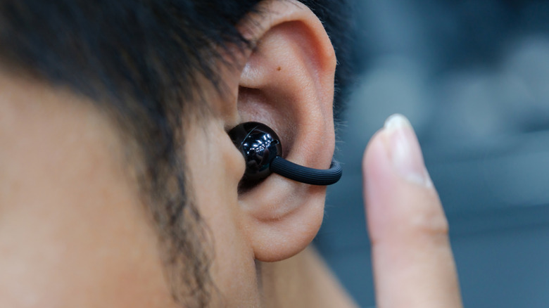 Close-up of a person wearing an open-ear wireless earbud with a hook design, curving around the side of the ear.