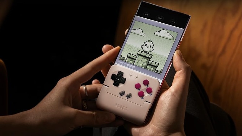A person holding a smartphone fitted with a retro-style gaming controller attachment while playing a pixel-art platform game.