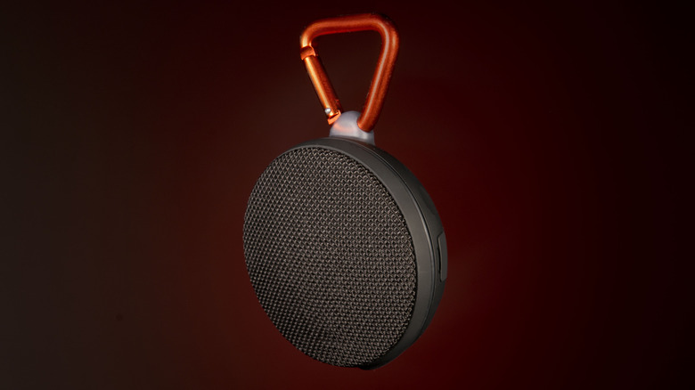 A portable clip-on Bluetooth speaker with a metal carabiner against a dark red background.