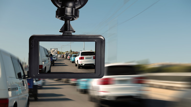 A dashcam mounted from a windshield on a heavy-traffic road. The cars in the backdrop are blurred as if speeding by.