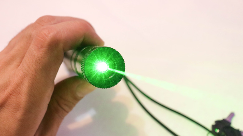 A hand holding a laser pointer that emits a green light towards the camera.