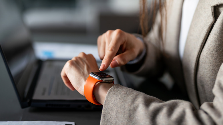 A businesswoman interacting with her orange smartwatch at a desk.