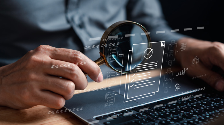An exaggerated depiction of data inspection on a laptop, with a person using a magnifying glass to inspect documents