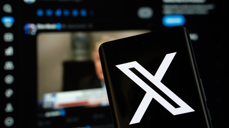 A phone displays the X Corporation logo with the browser version of the website blurred in the background.