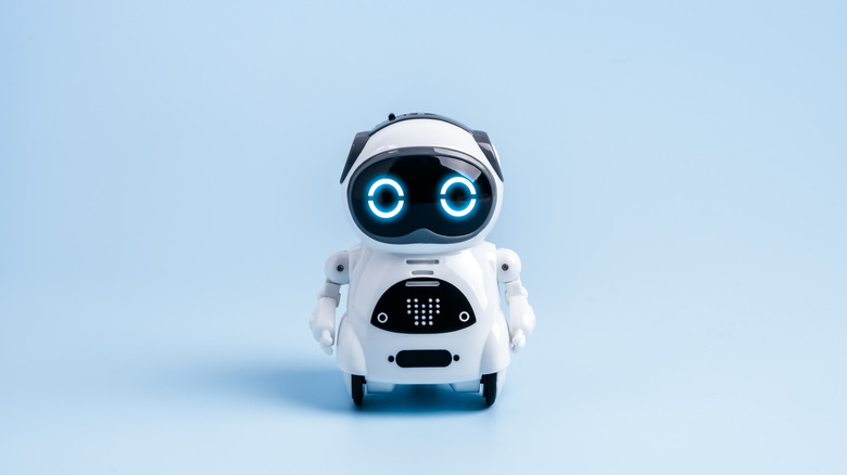 Small white toy robot with glowing blue eyes standing against a light blue background.