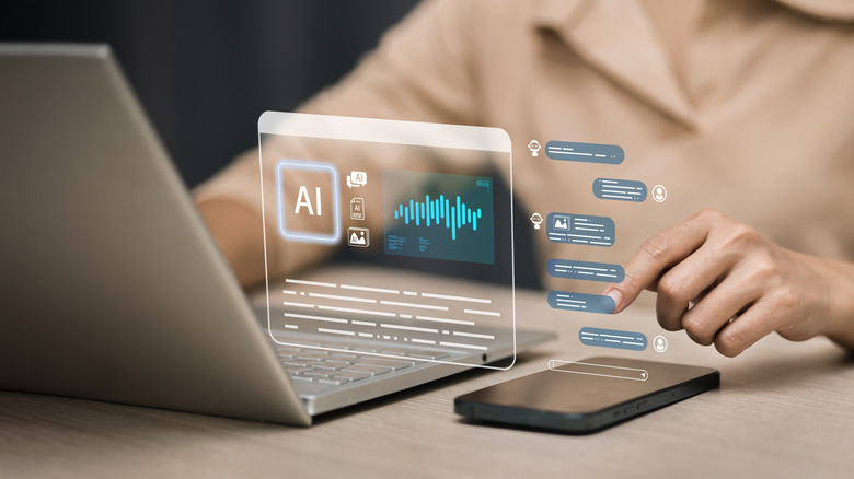 Person using a laptop and smartphone with floating AI interface graphics and chat icons displayed in front of the screen.
