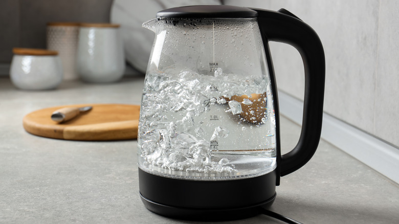 A glass electric kettle with boiling water on a counter top