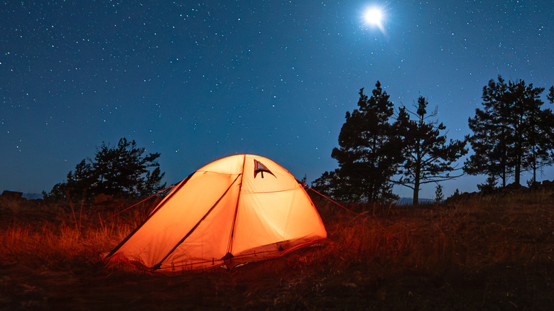 A tent illuminated by camping light at night under the stars