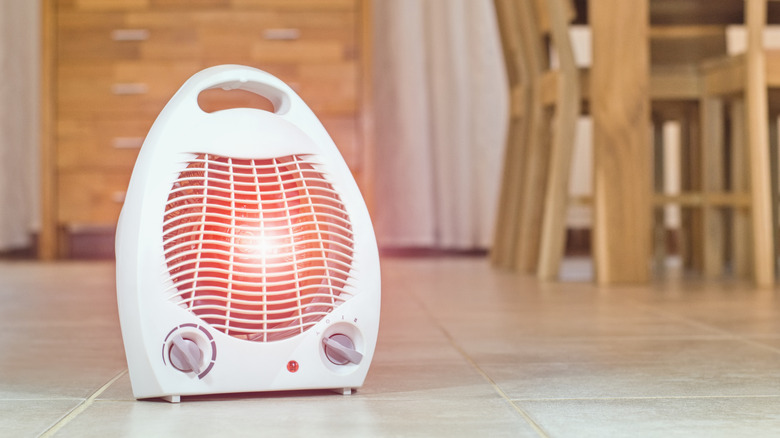 A white electric fan heater on a tiled floor