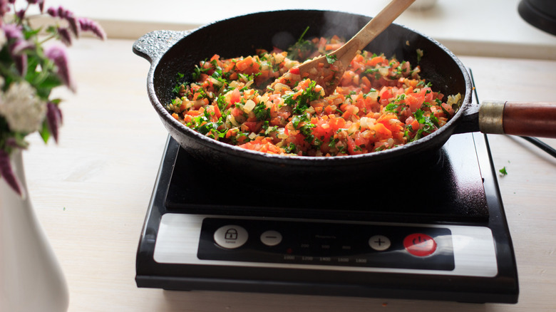 Portable induction cooktop cooking a meal on a cast iron pan