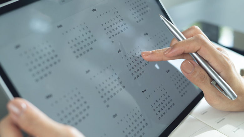 Close-up on a set of hands using a digital calendar app on a tablet.