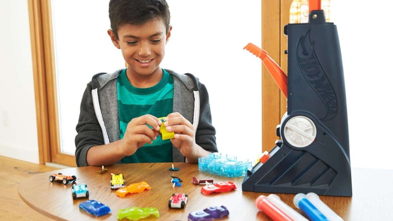 A child using the Hot Wheels Fusion Factory Car Maker on a brown wood table