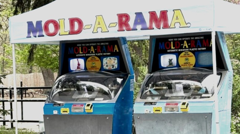 Two Mold-A-Rama injection molding machines under a white tent labelled "Mold-A-Rama"