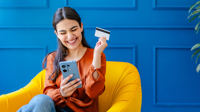A woman happily shopping on her phone, while holding a credit card.