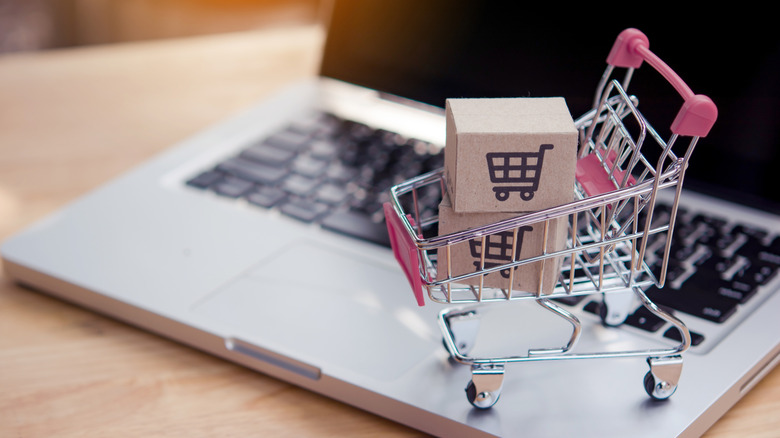 A mini shopping cart with boxes on top of an open laptop.