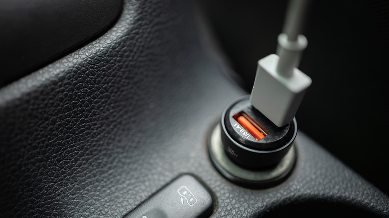 A close-up photo of a USB car charger plugged into a vehicle's 12V cigarette lighter socket