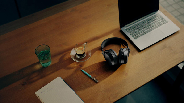 A pair of Sennheiser Momentum 5 Wireless headphones on a table with coffee and a MacBook.