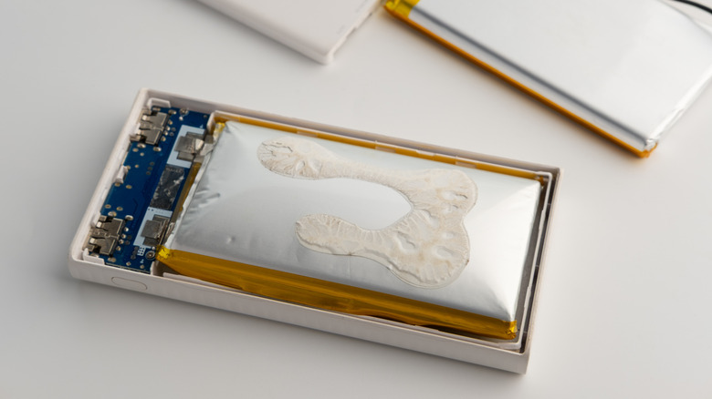Opened power bank exposing a severely swollen lithium-ion battery pressing against the casing, with the internal circuit board and charging ports visible.