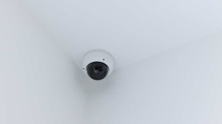 Dome-style security camera mounted on the ceiling in the corner of a room, positioned to monitor the surrounding area.