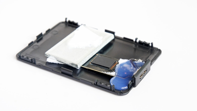 Disassembled fake portable SSD enclosure showing the internal circuit board, thermal pad, USB-C connector, and aluminum heatsink removed from the outer casing.