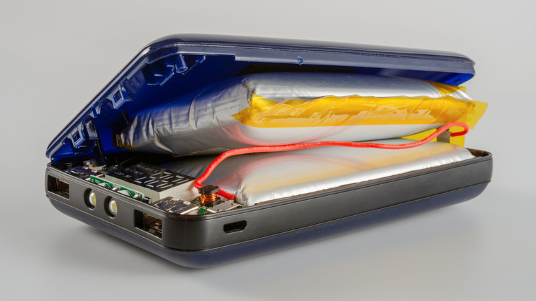 Opened power bank revealing two swollen lithium-ion pouch batteries bulging inside the plastic enclosure, exposing the internal circuit board and wiring.