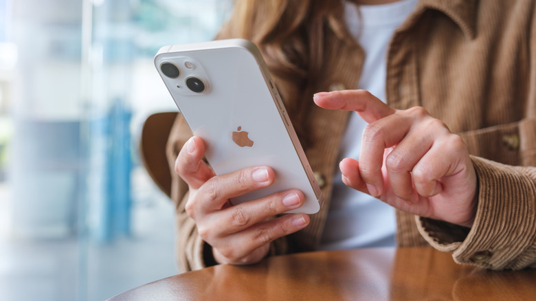 A woman holding and touching on iPhone 13 smart phone screen,
