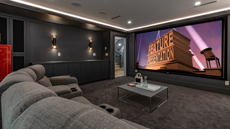 Luxurious home theater space with grey sofa, large screen, and dark walls