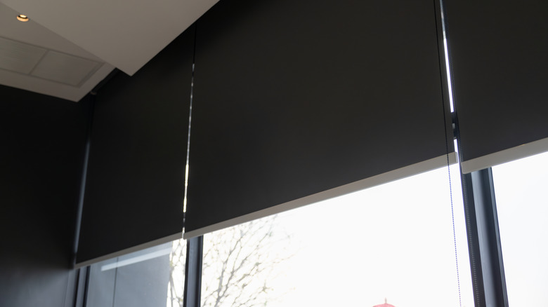A large window with blackout blinds pulled midway, blocking out most of the light from the bright day