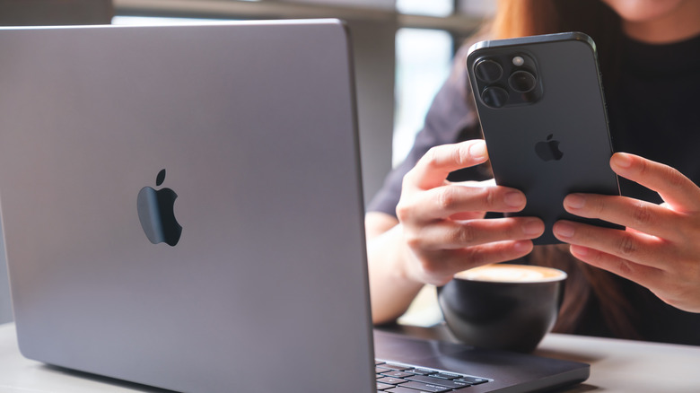 A person using their iPhone with a MacBook open in front of them.