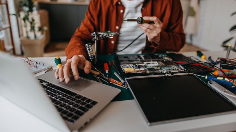 A person using a laptop while fixing a separate laptop with vaious tools in front of them.