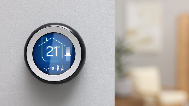 A digital thermostat showing the temperature of the house, placed against a wall