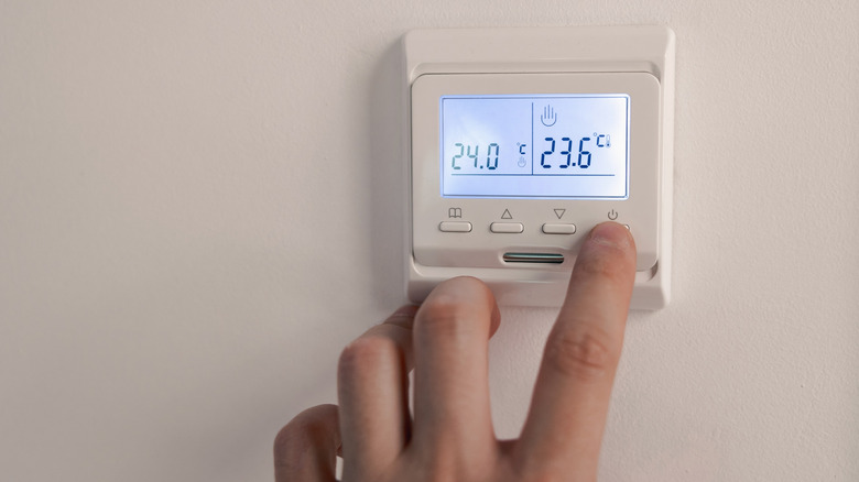 A person using the physical controls on their thermostat, which is showing the temperature