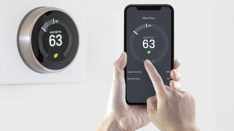 A person using their phone to control the temperature values of a smart thermostat