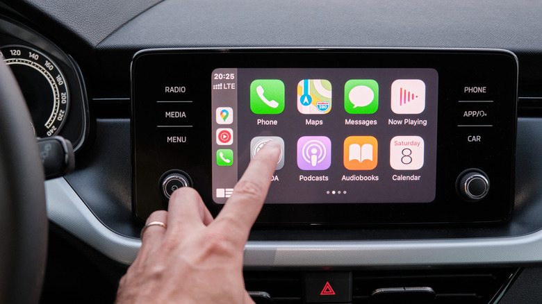 Close up of a hand touching an icon in the Apple CarPlay on car dashboard screen