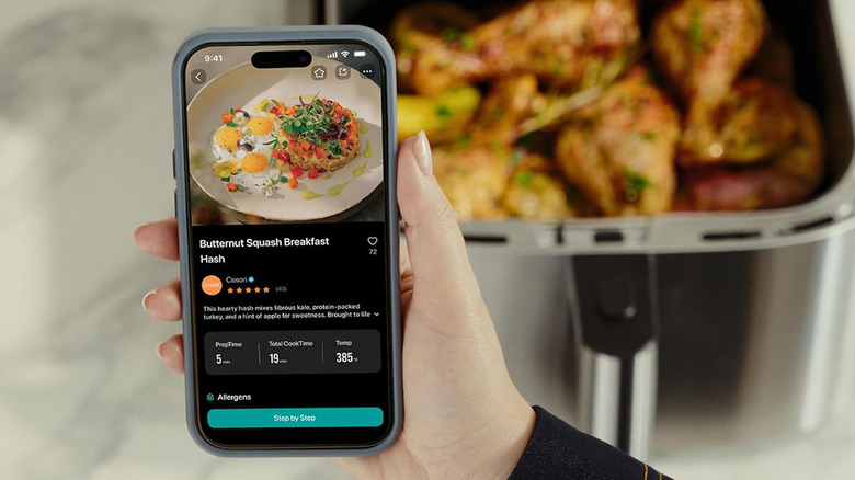 A person looking up a recipe on a cell phone with an air fryer in the background.