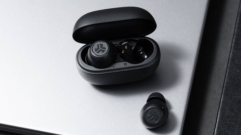 Black JLab Go Pop ANC earbuds placed atop a silver surface.