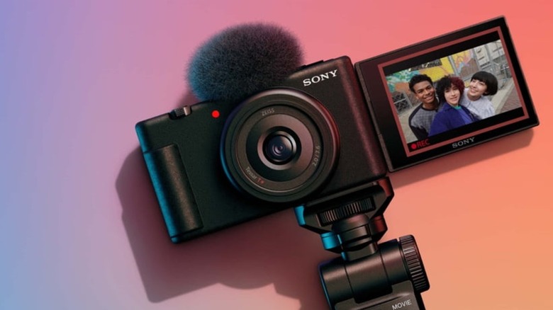 A Sony ZV-1F camera on a surface with a gradient background showing a selfie video recorded by three people