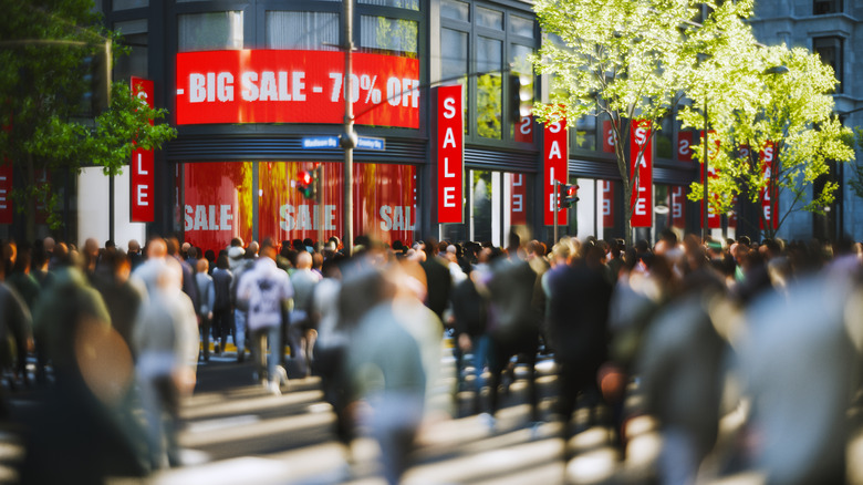 A realistic 3D render of a crowd in front of a storefront, red sale signs posted outside.