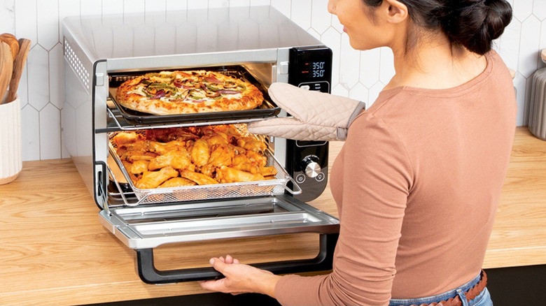 A woman using the Ninja DCT401 toaster oven to bake pizza and chicken.