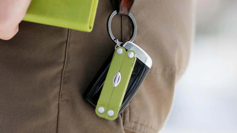A close-up of a person's waist shows a keyring clipped to a belt loop, holding a compact multi-tool.