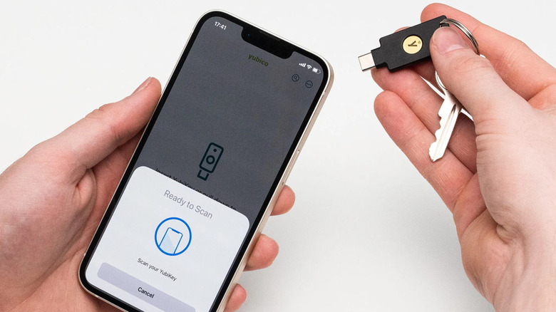 A person holds a smartphone displaying a "Ready to Scan" prompt while bringing a USB security key on a keyring close to it.