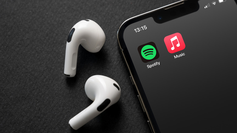 AirPods beside an iPhone with the Spotify and Apple Music icons on the screen.