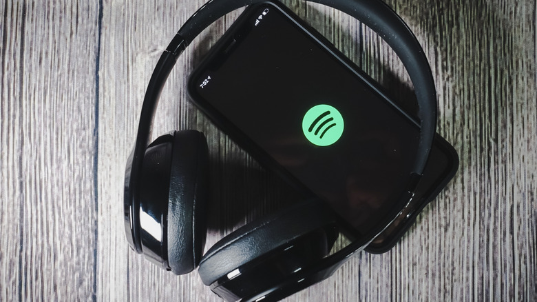 Headphones placed on top of a smartphone with the Spotify logo on the screen.